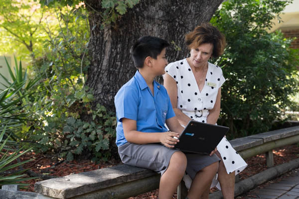 St Raphael South Hurstville Principal sitting on bench with student looking at laptop